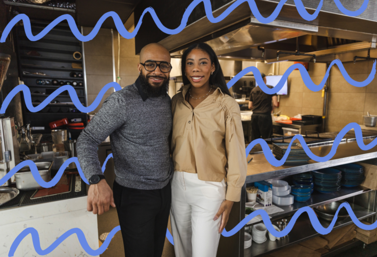 2 restaurant owners standing in front of a busy restaurant kitchen.