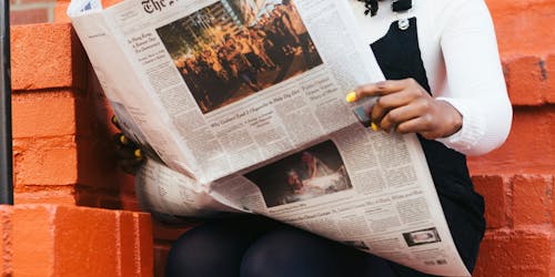 Person reading New York Times against backdrop of a brick wall