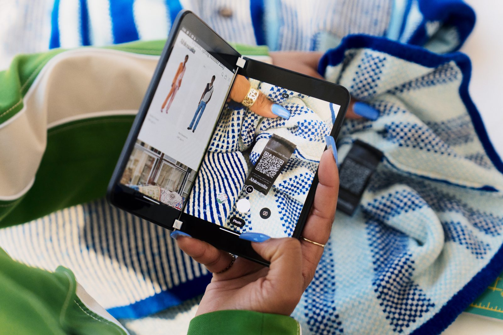 A photo of a woman using a phone (a Microsoft Surface Duo) to take a photo of a QR code on a label of a blue Alhuwalia top