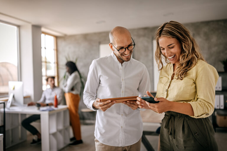 Smiling man and woman collaborating on devices in office