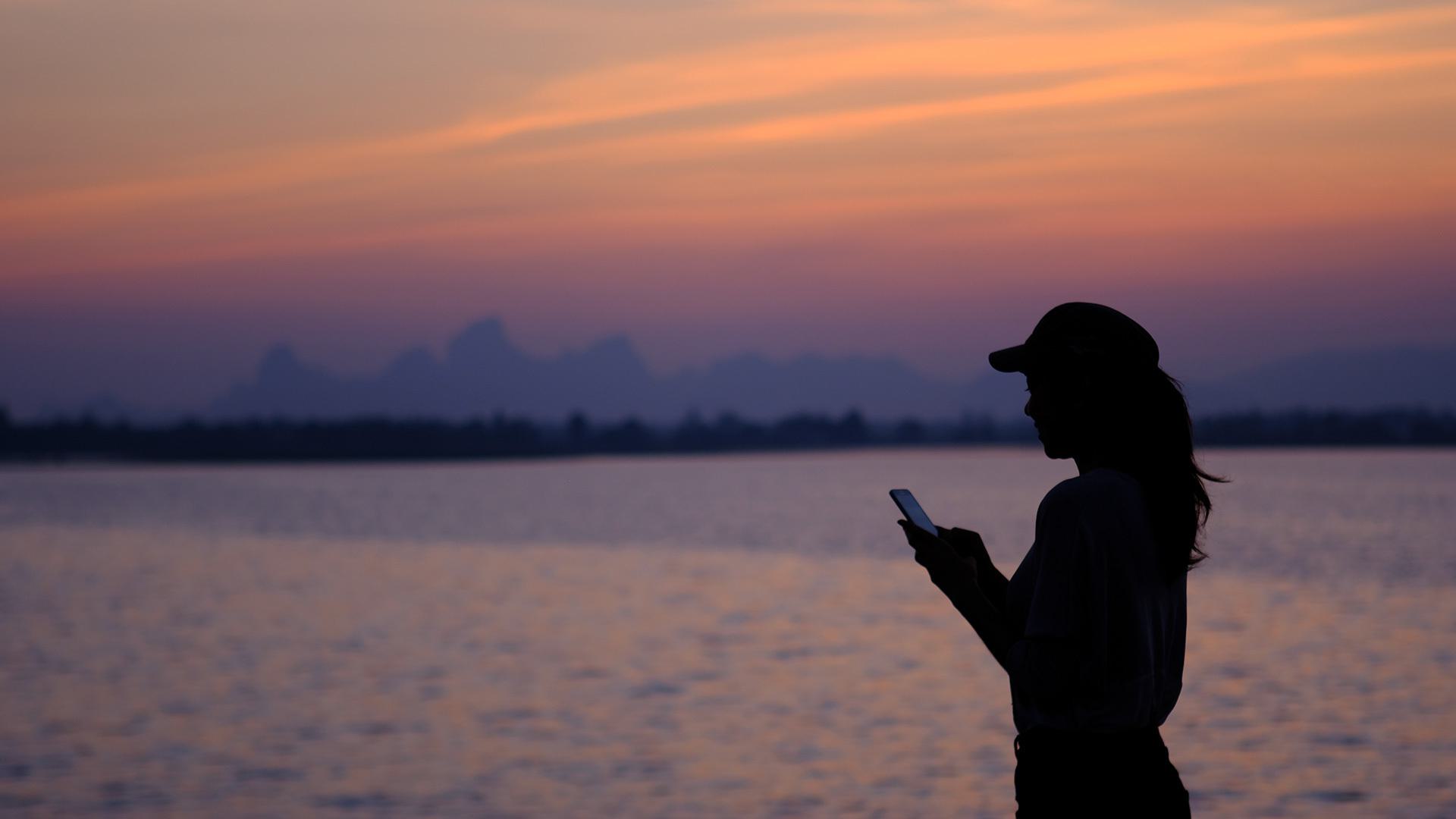 woman at sunset by lake with phone