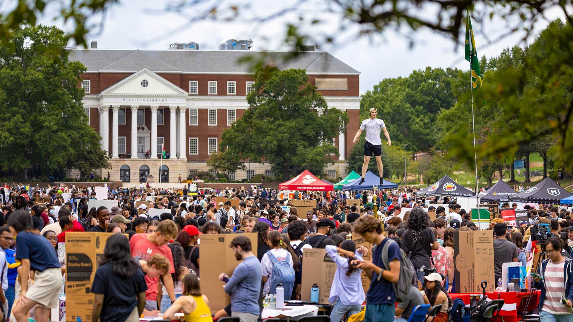 student leaps above crowd and tents on McKeldin Mall during First Look Fair