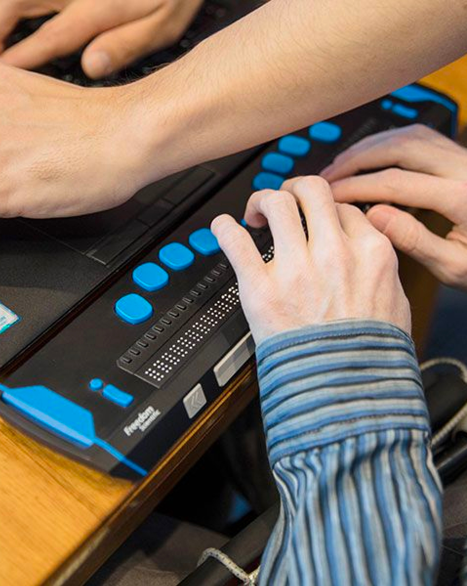 Hands of several people using a modern, blue-buttoned digital audio mixer in a studio setting.