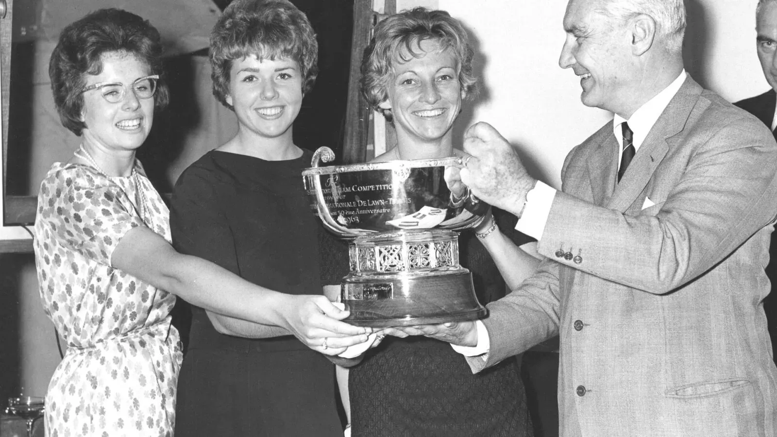 Three women and one man hold a trophy together.