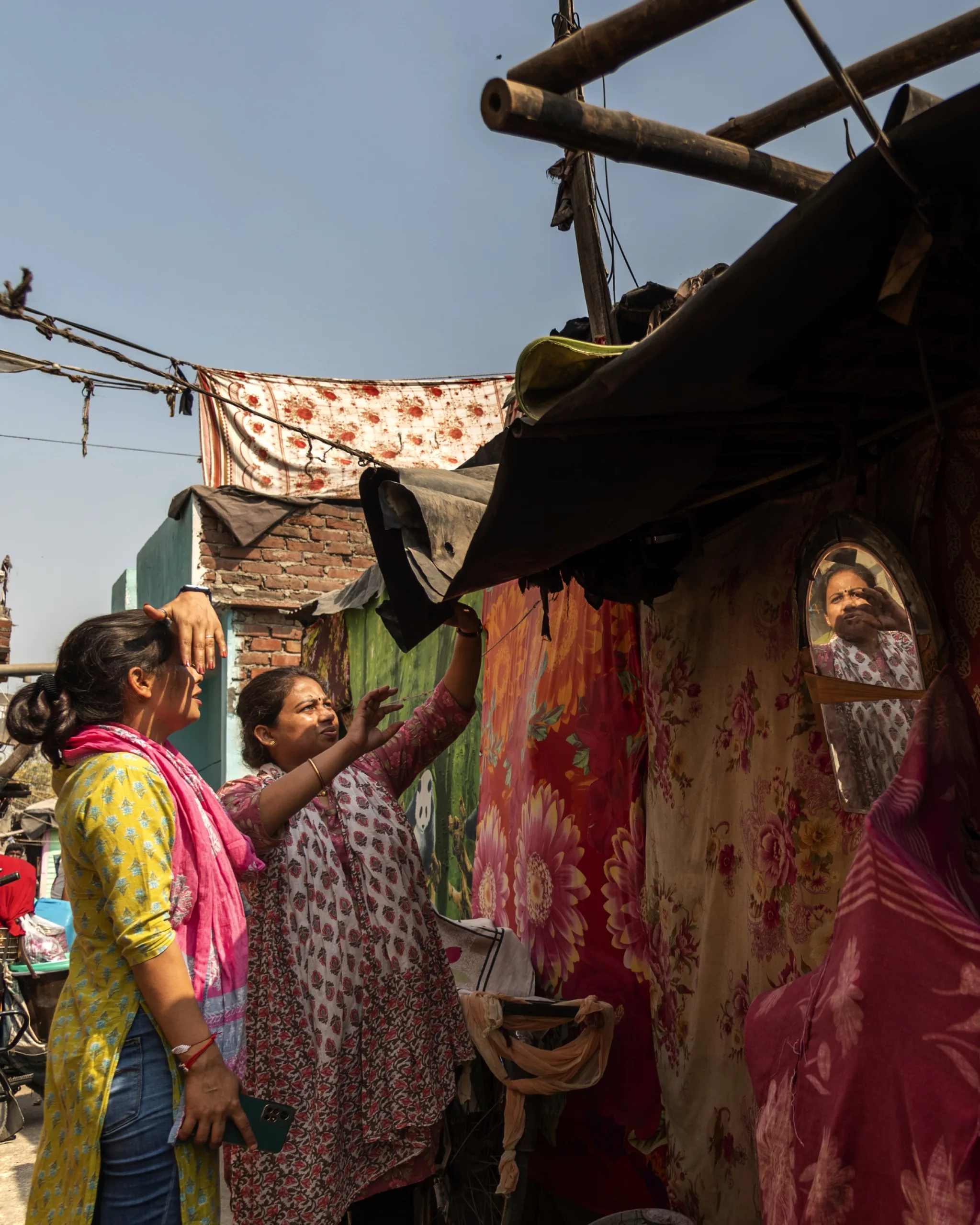 A woman stands outside of a home in a densely packed neighborhood and points to its roof.