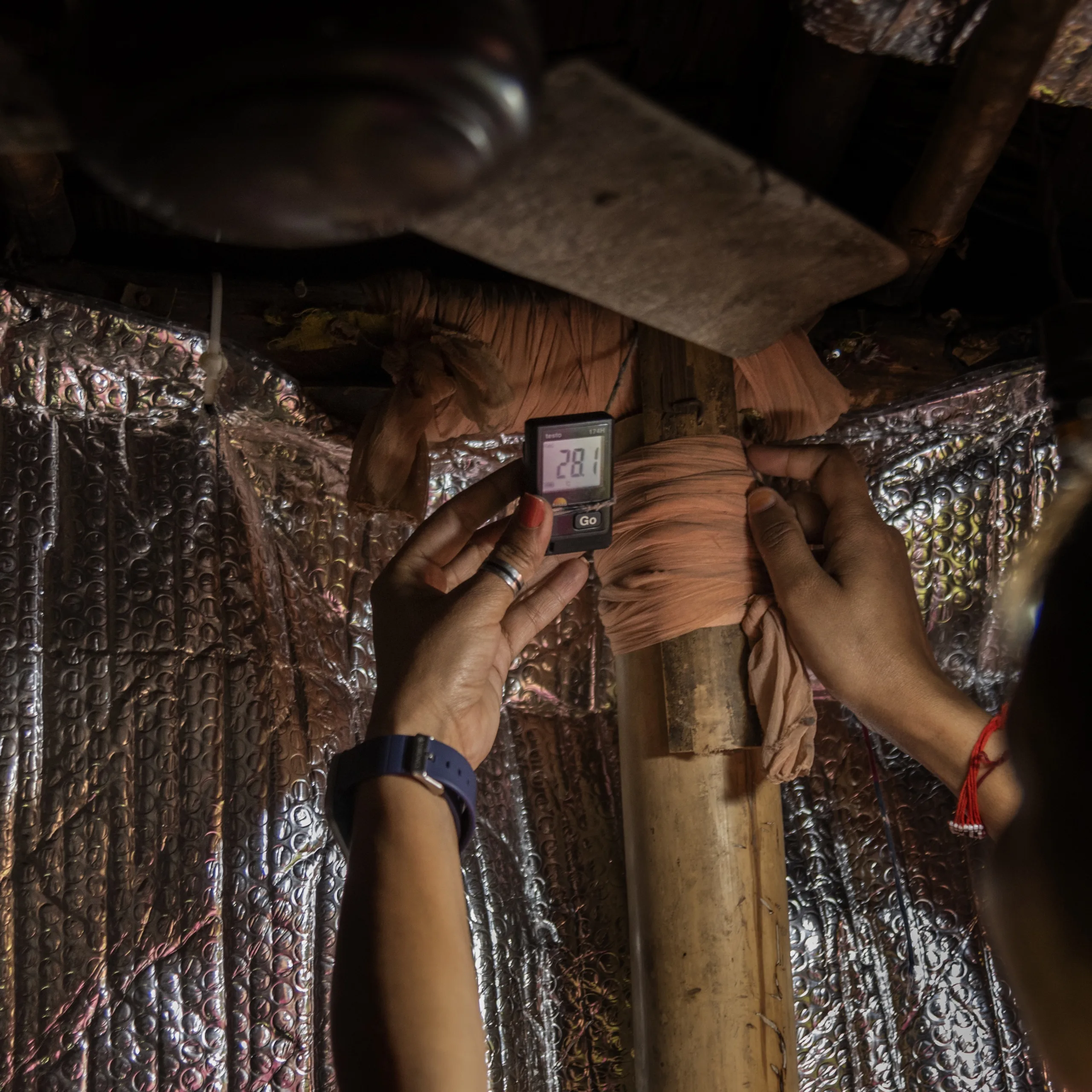 A woman looks at the insulation inside of a home while a mother and child look on from the doorway. 