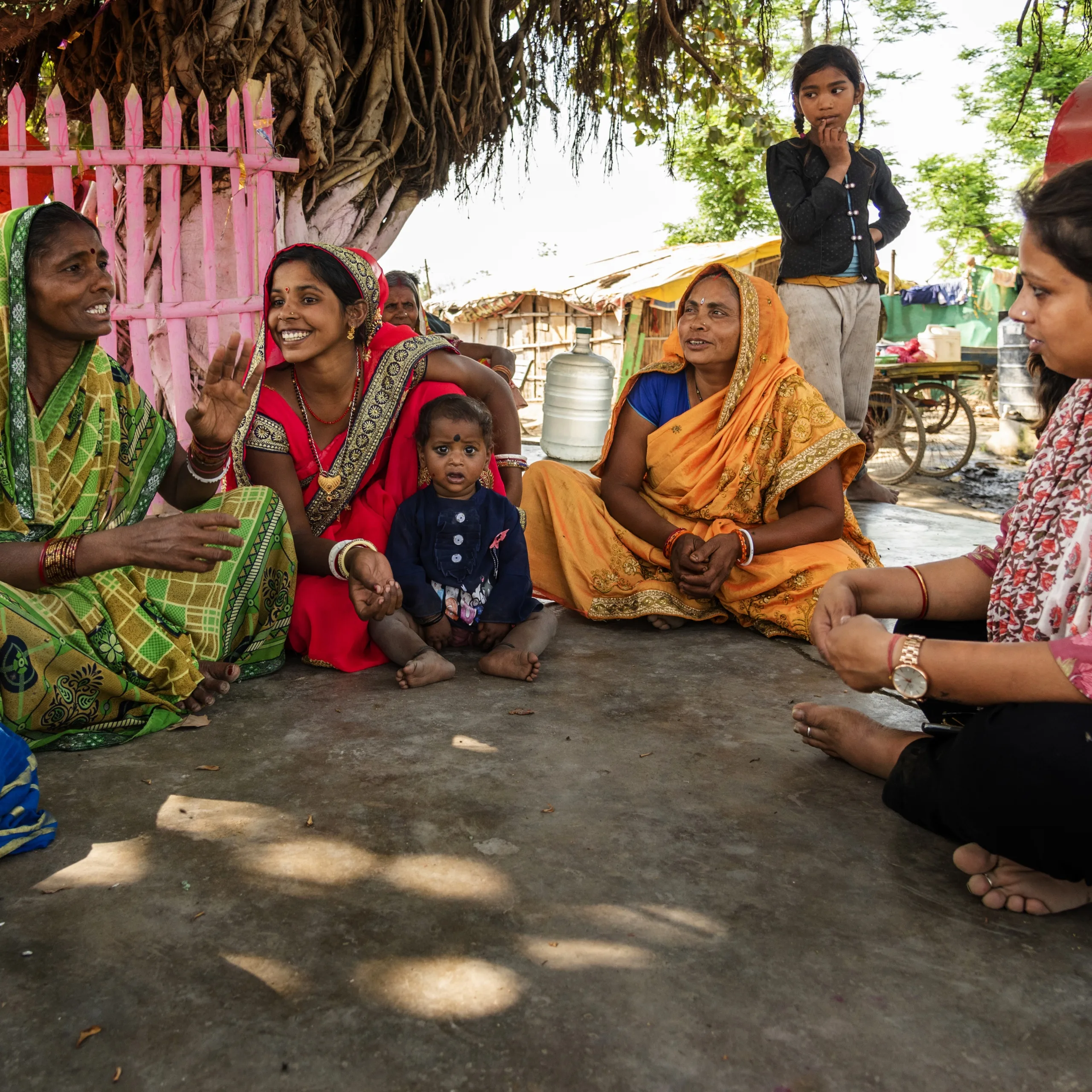 A group of women talk with each other while sitting in the shade.