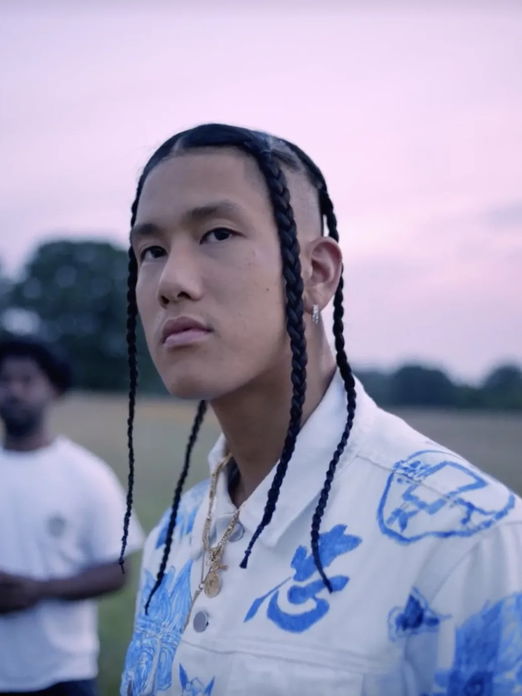 Closeup image of Spence Lee looking at the camera with a pink sky and blurry trees in the background.