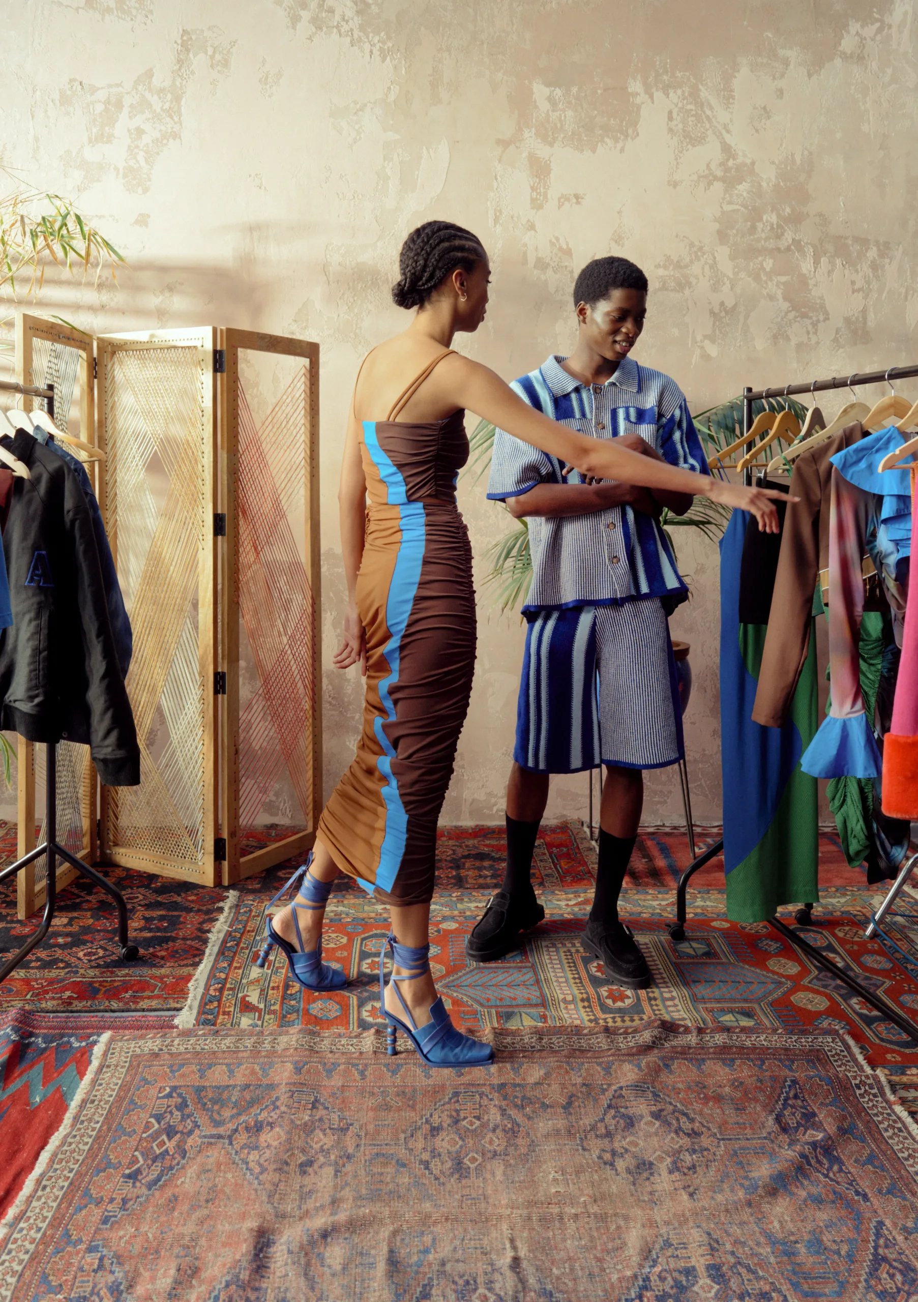 A man and woman standing next to a rack of clothes.