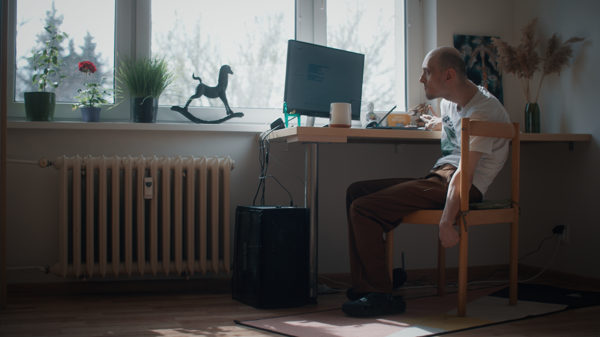 A man sitting at a desk, writing code on a computer. Natural light pours in from large windows.