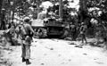 On the Ginowan road, men and armor of the 382d Infantry, 96th Division, move through a wooded area.