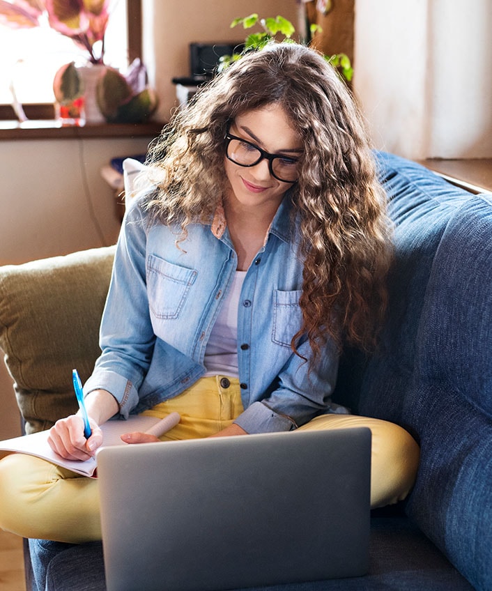 A woman taking notes on how to free up RAM while looking at a laptop.