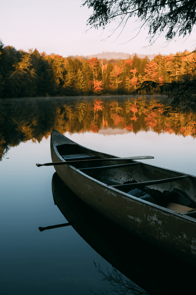 A canoe sits in a still lake. Orange trees surround the lake and reflect on the water's surface.