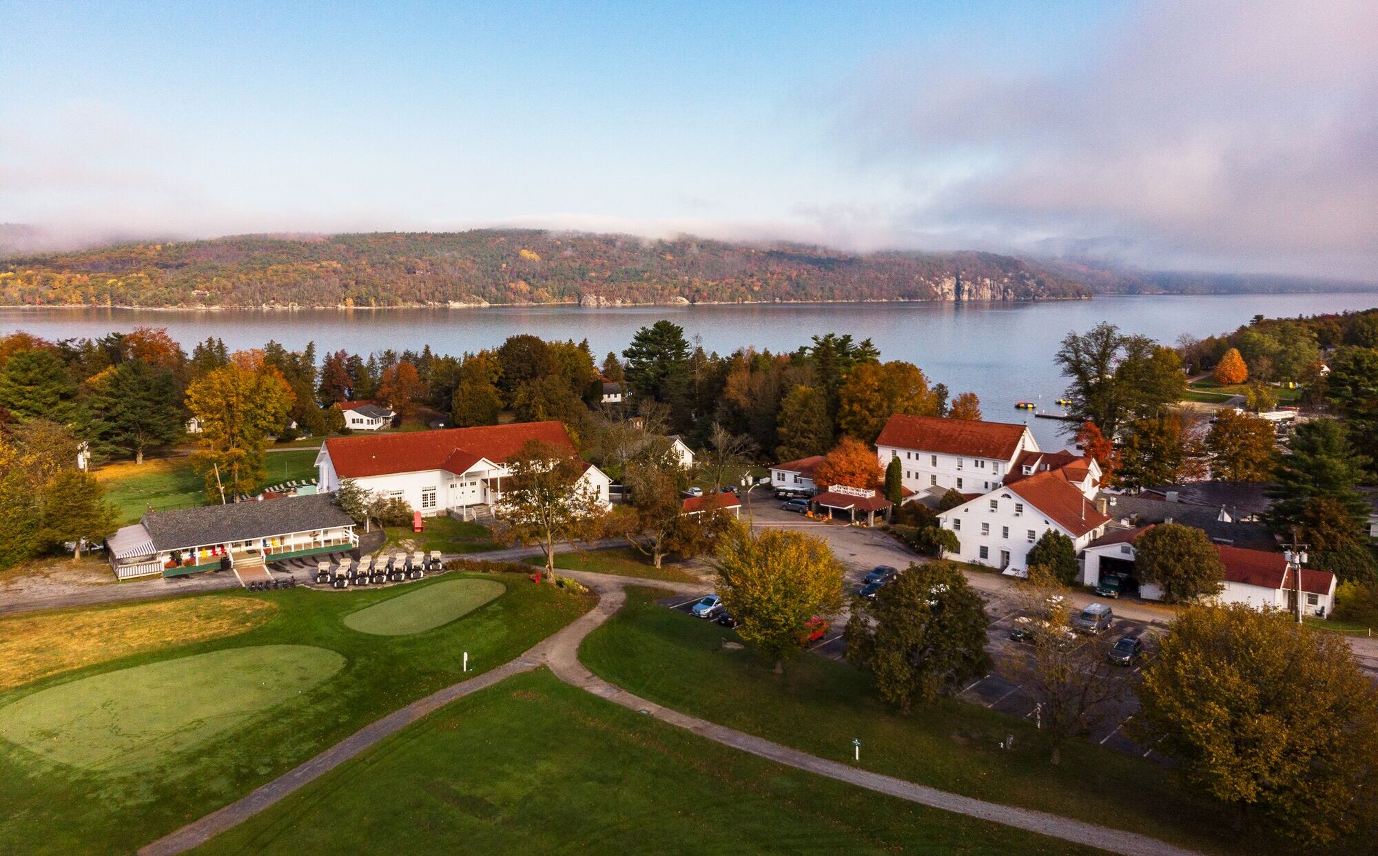 Seen from above, a white building with a red roof bordering a large lake.