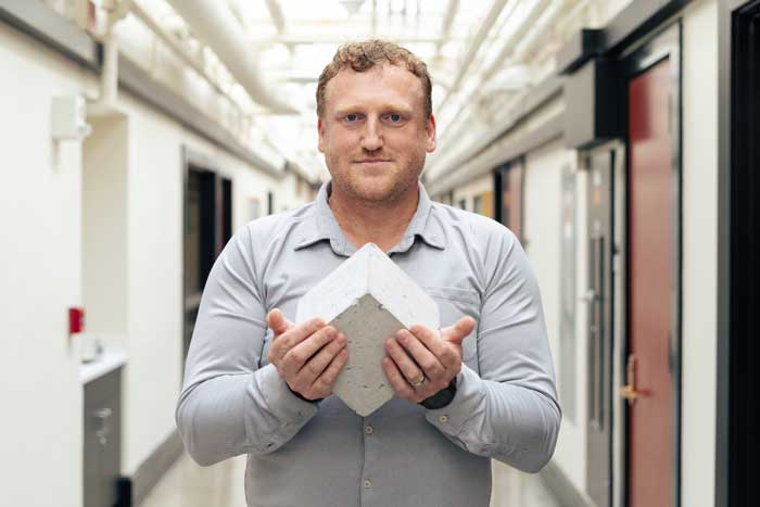 Admir Masic holds a cube of cement in a hall at MIT