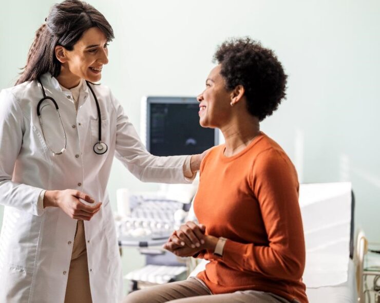 A smiling doctor talking to a patient, reassuring her with her hand on her shoulder.