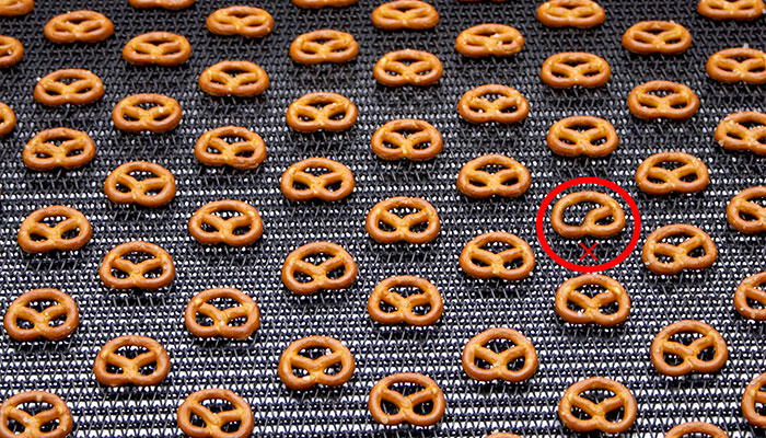 Um sistema de visão identifica um pretzel defeituoso em uma linha de produção.