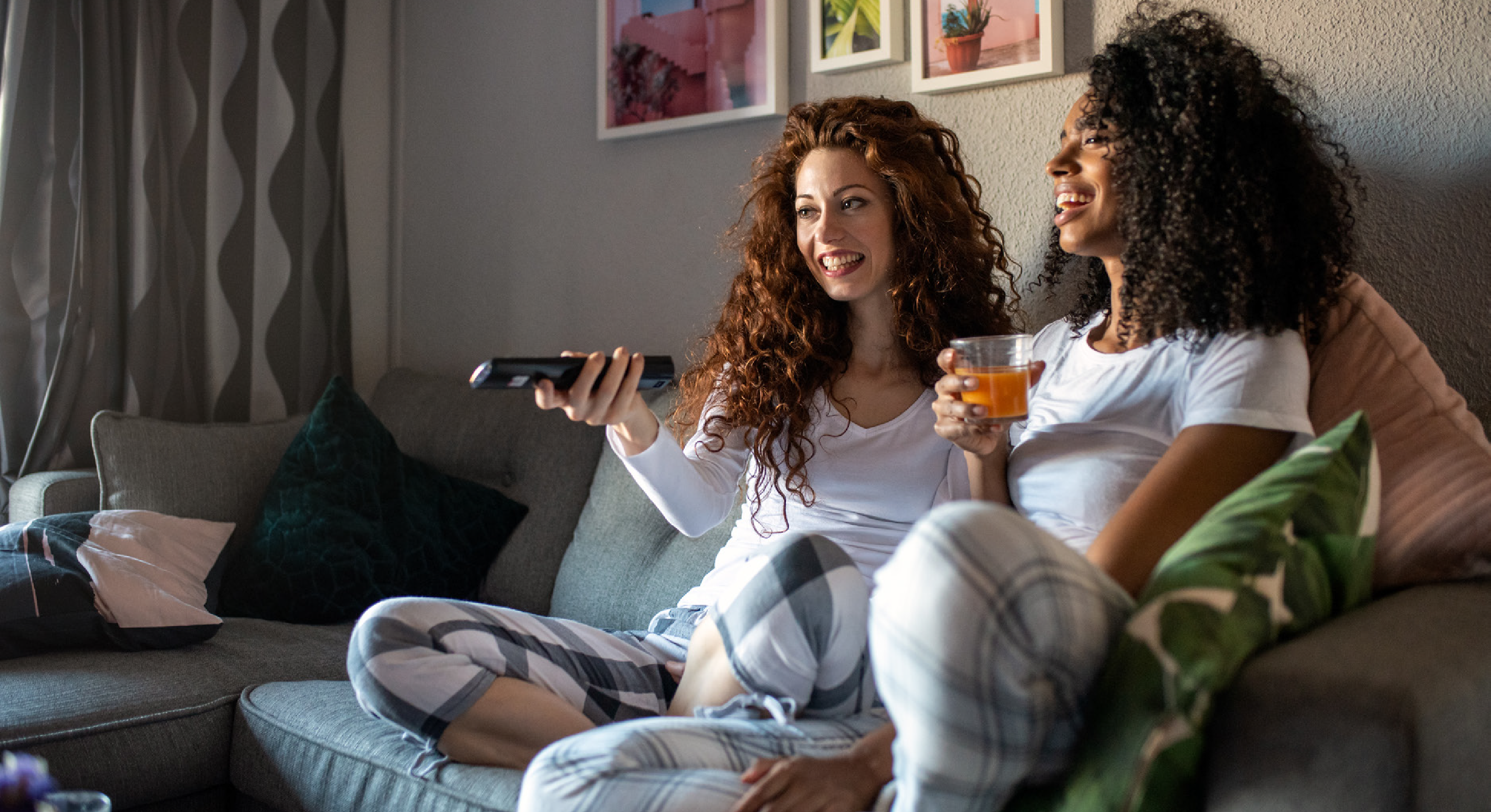 two women sitting and having remote and juice in hand