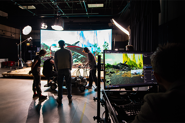 a virtual production set with large screen in background showing spaceship and performers and filmmakers in foreground