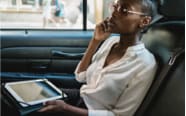 woman riding in the back seat of a vehicle speaking on cellphone while holding a tablet