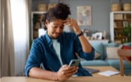 man rubbing his forehead while checking his cellphone