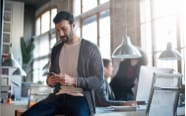 man sitting on a desk while checking his cellphone