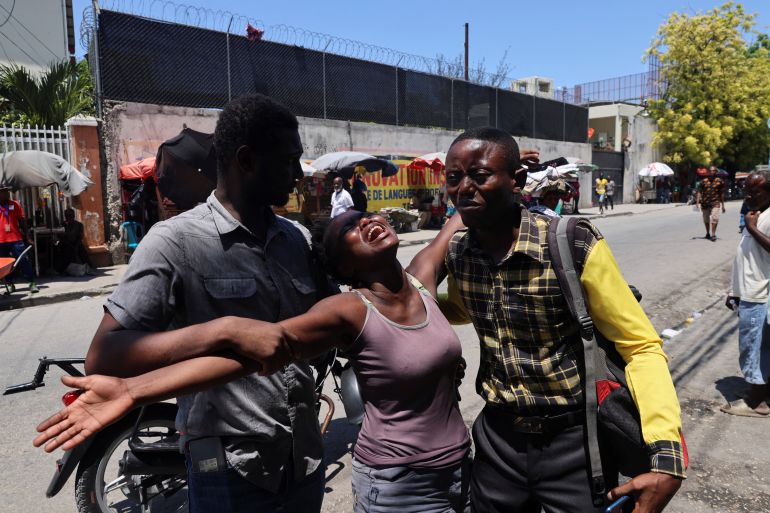 A Haitian woman is helped by others as she reacts upon seeing the dead body of her brother