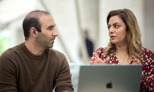 Desireh, seated in front of a MacBook, speaking with a colleague