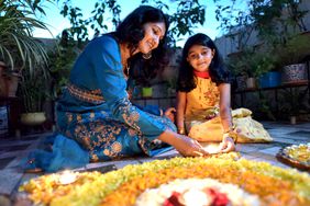 Mother and daughter lighting lamps around rangoli during Diwali