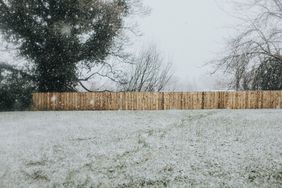 Garden Covered in Snow. Untreated wooden fence in the distance.