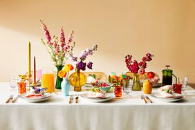 spring colored tablescape with butterfly napkin rings, colorful tumblers, pink, purple, yellow and red flowers in vases on white tablecloth with white dinnerware