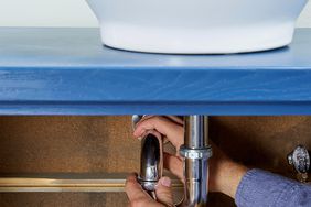 man adjusting plumbing underneath pedestal sink basin