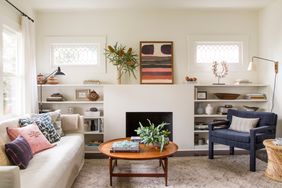 living room with modern fireplace surround flanked by bookshelves, original leaded-glass windows, white sofa, rug, and round coffee table