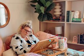 Woman coloring on a pink couch with bookshelves and a plant