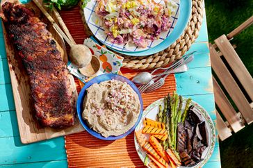 outdoor picnic table of ribs, hummus, salad russe, and grilled vegetables