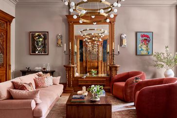 living room centered around dark brown coffee table with light fixture aboce, large mirror, pink couch, and two red rounded chairs