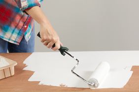 close up of a woman painting with a roller on a wooden surface