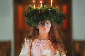 girl holding candle while wearing traditional wreath on head with lit candles in celebration of St. Lucy's Day