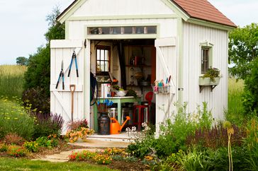 White garden shed with doors open to view of worktable and gardening tools