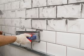 grouting mistakes; person grouting white subway tile in kitchen