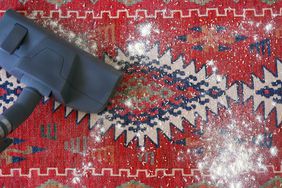 overhead shot of a vacuum cleaner cleaning a red handwoven carpet with carpet cleaning powder