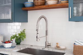 marble counter kitchen sink with blue cabinets and decorative bowls on wood shelves