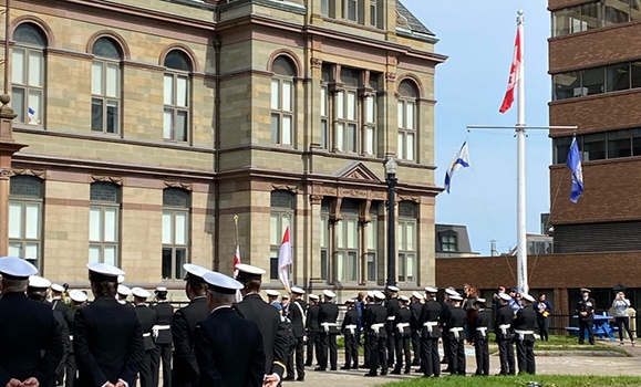 Members of the Canadian naval reserves are standing in formation outside City Hall in Halifax’s Grand Parade Square with the Canadian flag flying.