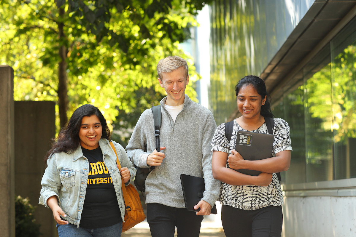 Three computer science students on Dal campus with building and foliage in background.