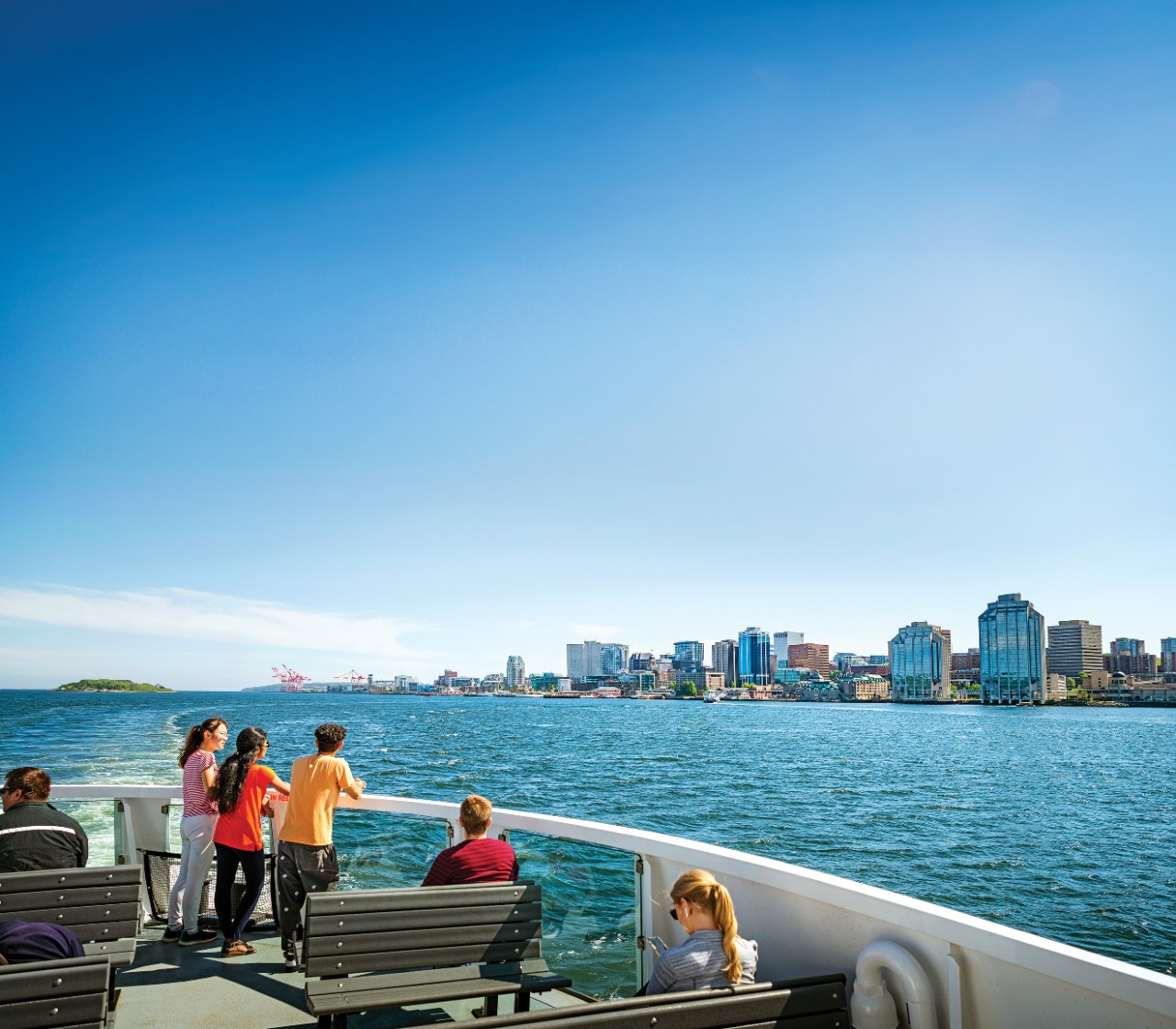 A group of 3 students on the top deck of the ferry with Halifax skyline in the distance.