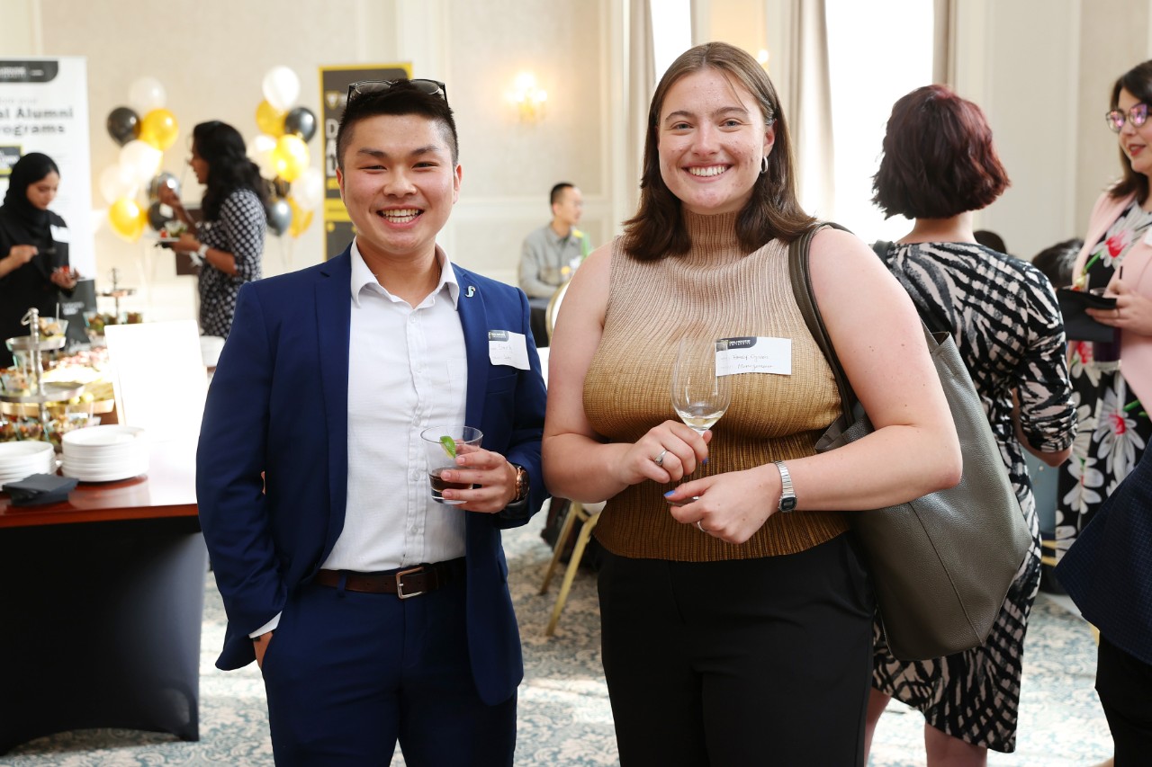 Two people posing for a photo at an event in a hotel meeting room dressed for business casual.