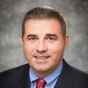 Photo of Barry Carter, podcast episode guest. Wearing dark suit, blue shirt, red tie.