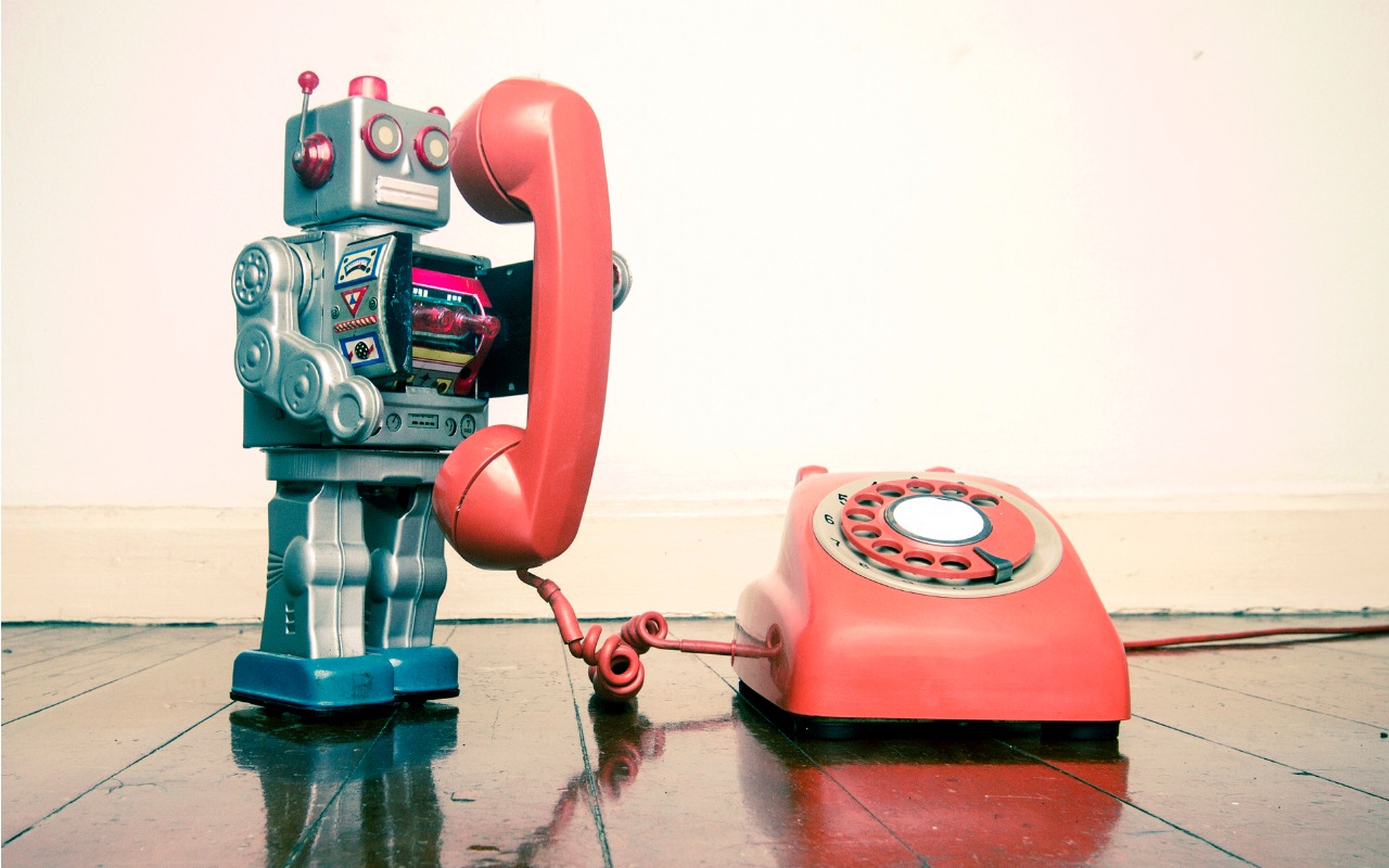 Silver robot toy holding the receiver of an old rotary dial telephone.