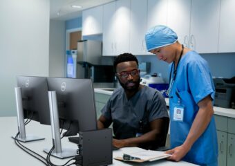 Male and female medical professionals confer about patient case with Dell Optiplex 3000 Thin Client and P2422H monitors on desk in front of them.