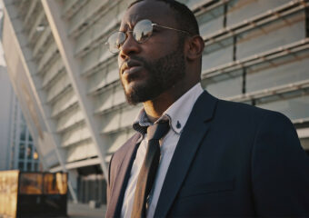 African-American businessman in suit, tie and glasses as he exits a building.